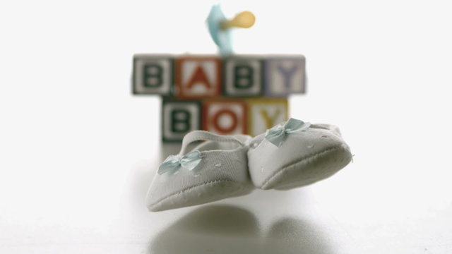 Baby shoes falling in front of blue soother and baby blocks