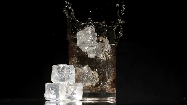 Ice cubes falling into glass of whiskey and ice next to