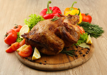 Whole roasted chicken with vegetables on plate, on wooden table