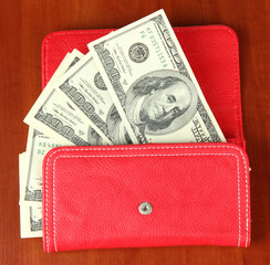 Purse with hundred dollar banknotes, on wooden background