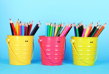Colorful pencils in three pails on blue background