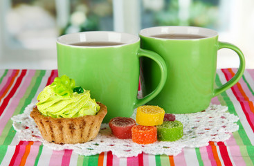 Cups of tea with cake and candy on table in room