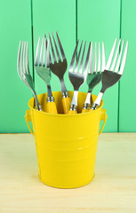 Forks in metal bucket on color wooden background