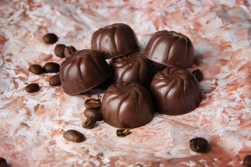 Chocolate candies and coffee beans, on color background