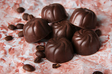 Chocolate candies and coffee beans, on color background
