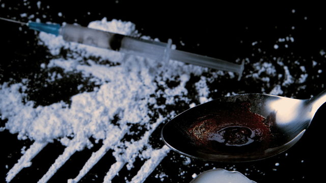 Syringe falling on white drug while drug is cooking on spoon