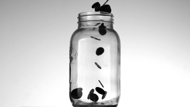 Many coins pouring into glass jar on white background