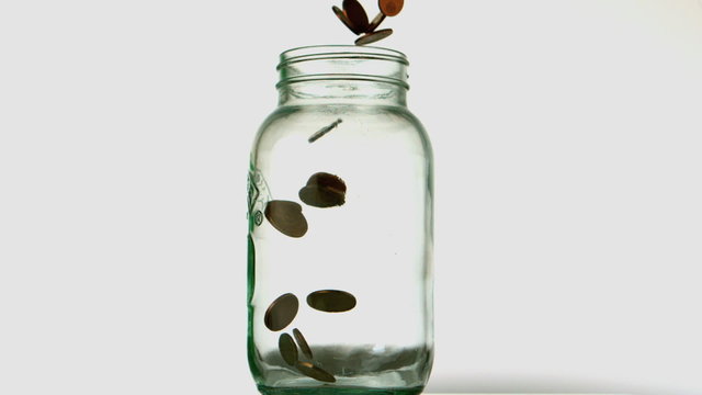 Coins pouring into glass jar on white background