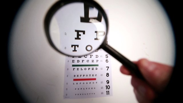 Someone holding magnifying glass up to eye test