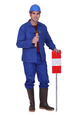 Construction worker standing with a mallet and traffic sign