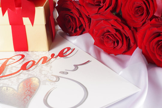 golden gift box and red roses on white satin background