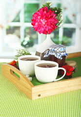 Cups of tea with flower and jam on wooden tray on table in room