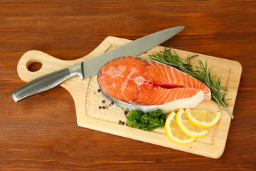 Fresh salmon steak on cutting board, on wooden background