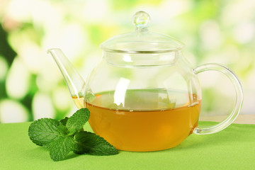 Teapot with mint on table on bright background