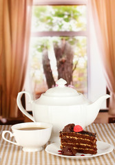 Teapot, cup of tea and delicious cake on window background