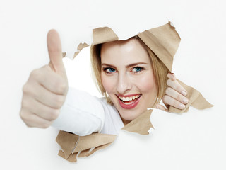 Pretty woman with thumb up looking through paper hole