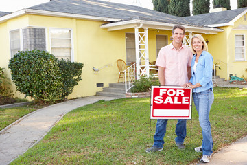 Couple Standing By For Sale Sign Outside Home