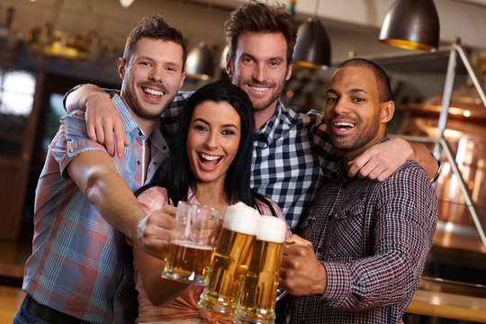 Group of happy friends clinking with beer in pub
