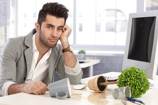 Desperate businessman sitting at desk in disorder