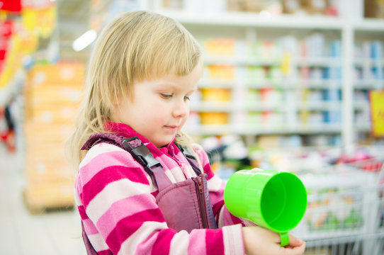 Adorable girl on shopping cart with green cup in supermarket