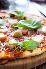 thin pizza with bacon, olives and basil on board