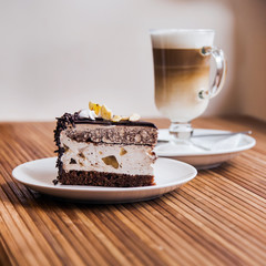 A piece of chocolate cake, coffee in the background