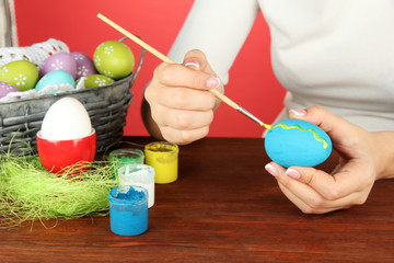 Fototapeta na wymiar Young woman painting Easter eggs, on color background