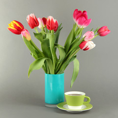 Fototapeta na wymiar Beautiful tulips in bucket with cup of tea on grey background