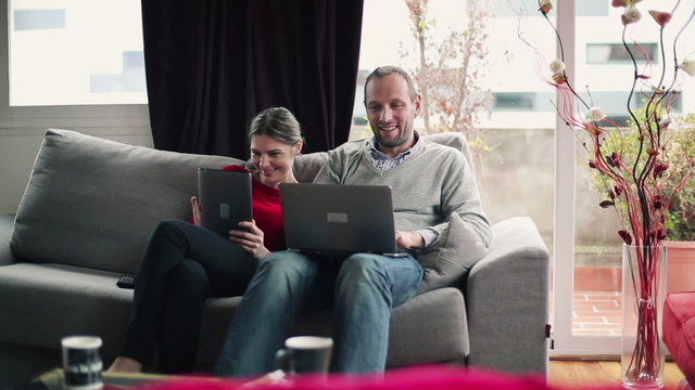 Happy couple with laptop and tablet computer on sofa