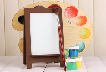 Photo frame as easel with artist's tools on wooden background