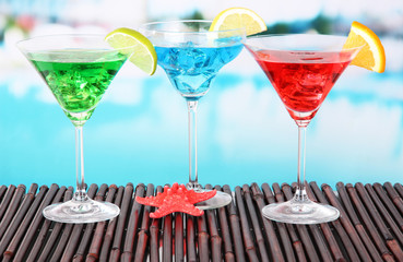 Glasses of cocktails on table near pool