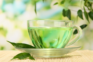 Transparent cup of green tea on bamboo mat, on nature
