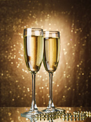 Two glasses of champagne on bright background with lights