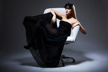 Relax. Woman relaxing in Chair. Black Dress, Mask with Feathers