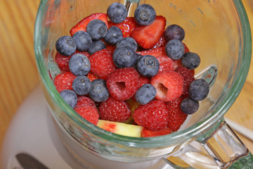 Fruit, including blueberries, raspberries, strawberries and pineapple, in a blender, about to made into a smoothie.