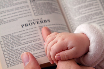 Baby Holding Dad’s Finger on Bible - obrazy, fototapety, plakaty