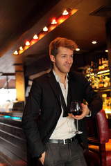 Happy young man in a black suit holding a glass of wine