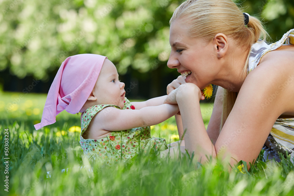 Wall mural Young smiling mother plays with her baby on grass