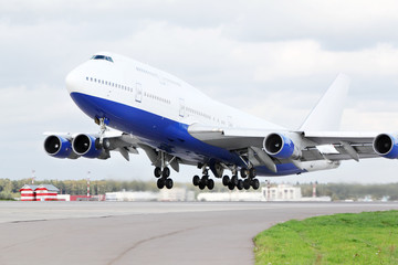 Large blue and white passenger airplane takes off at airport.