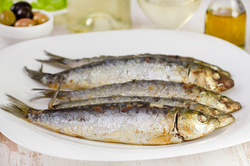 fried sardines on the plate with glass of wine