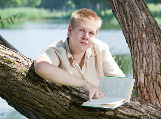 The young man  reads the book on the river bank..