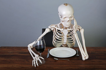Skelett vor leerem Teller mit einem Glas Rotwein