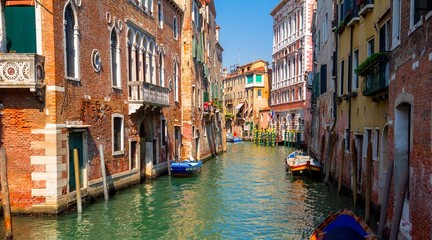 Naklejka na ściany i meble Sunny channel in Venice with boats parked around.