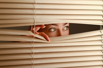 Portrait of a woman looking through out the blinds