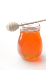 Jar of honey with wooden drizzler isolated on white background