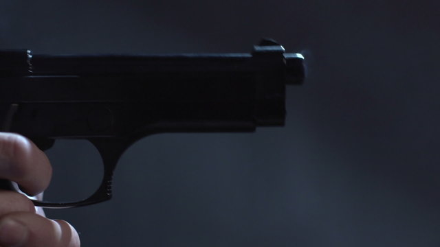 Close profile of man holding a 9 mm handgun, then takes a shot