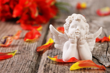 Weißer Engel mit aufgestützten Händen vor roten Blüten