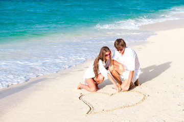 Fototapeta premium young happy couple drawing heart on tropical beach. honeymoon