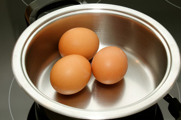 three brown eggs in a pan of water