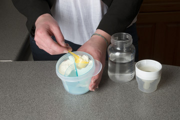 Young mother's hands preparing powdered milk drink for her baby